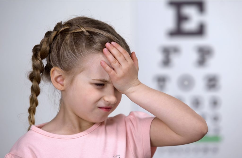 A little girl standing in front of a Snellen eye chart suffering from a headache, a symptom of myopia