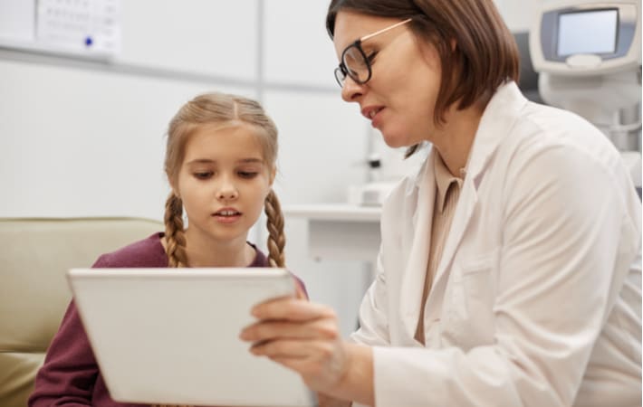 A little girl with her optometrist looking at a tablet discussing how to treat her lazy eye