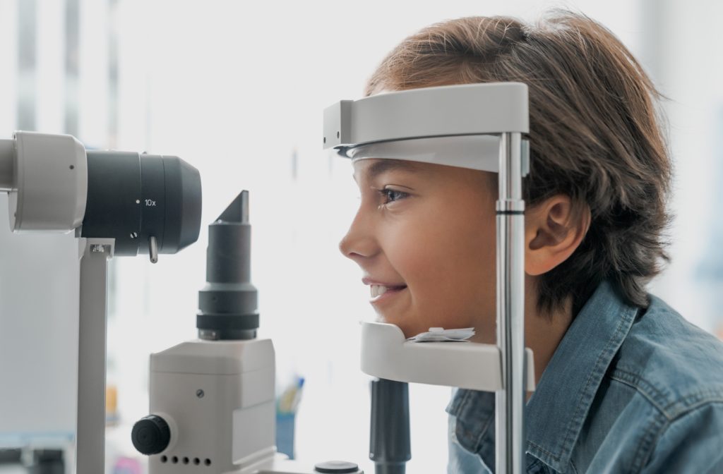 A side view of a young boy smiling at his optometrist getting an eye exam with his chin on a tonometer.