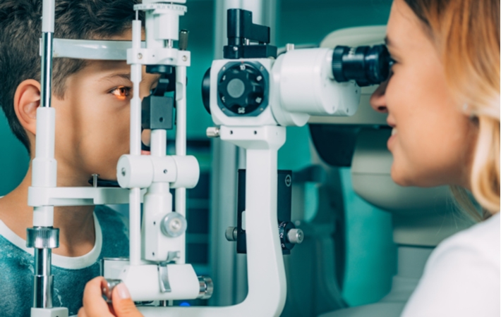 An optometrist performing a slit lamp test on a young boy as part of his regular eye examination