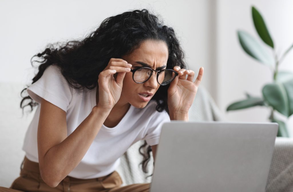 A woman squinting bent over trying to get as close as possible to her computer screen as she struggles to see indicating that her glasses prescription could be wrong