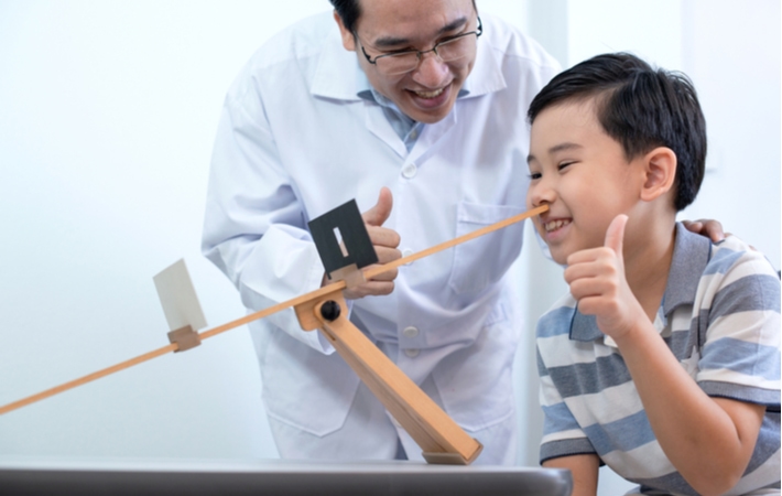 A young boy performing vision therapy exercises, giving the thumbs up to his optometrist who is standing close watching