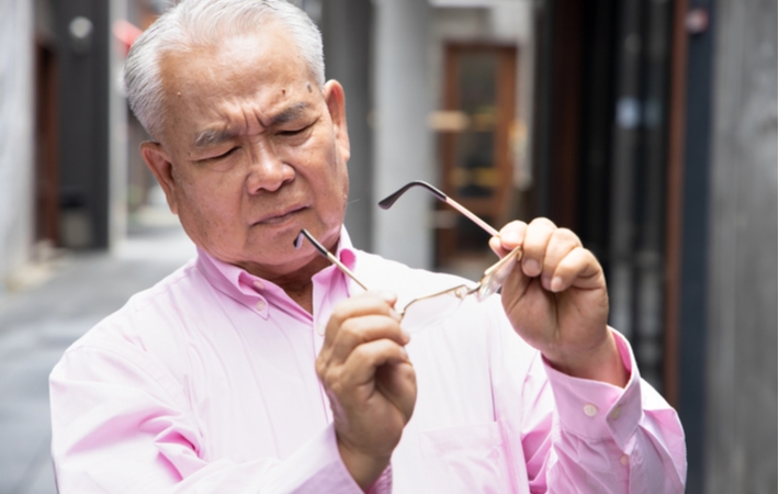 A man taking off his glasses and looking at the lenses with confusion as he is experiencing vision issues because of an outdated prescription