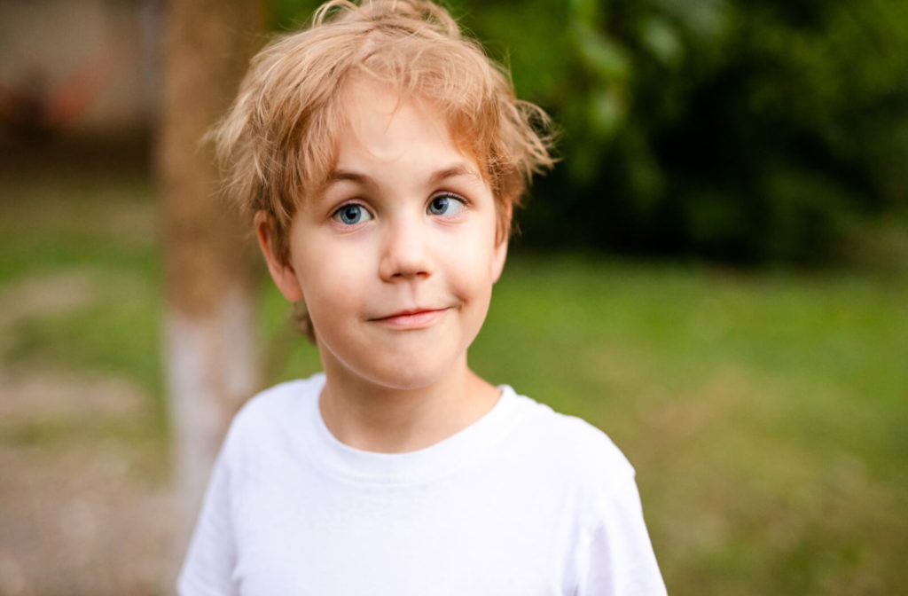 Alt text: A boy with strabismus standing outside with a white shirt