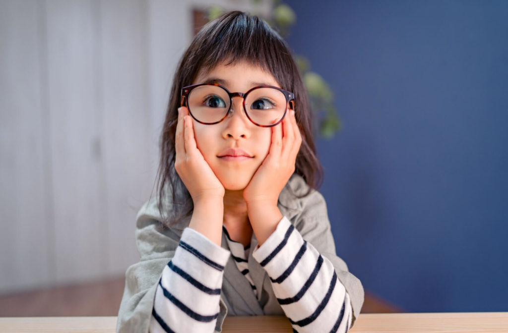 A young girl with amblyopia wearing glasses for the first time while she rests her head on both of her hands