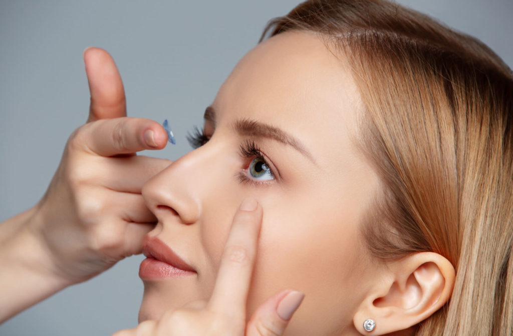 A close-up of a young woman with a toric contact lens on the tip of her right index finger about to insert the lens on her eye.