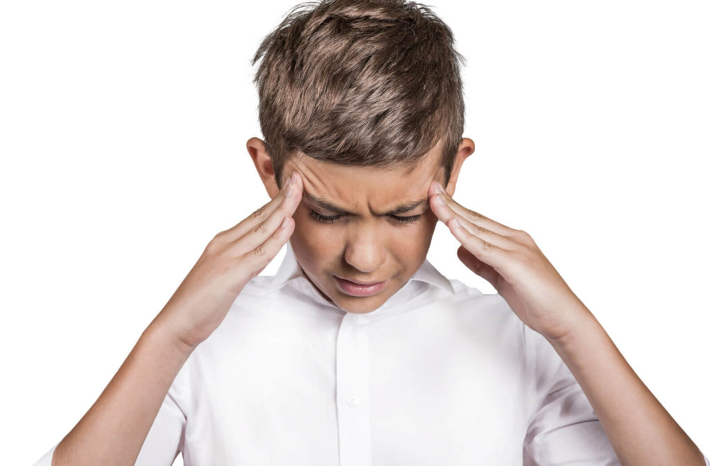 A boy in a white shirt is massaging his temples to relieve pain from a headache.
