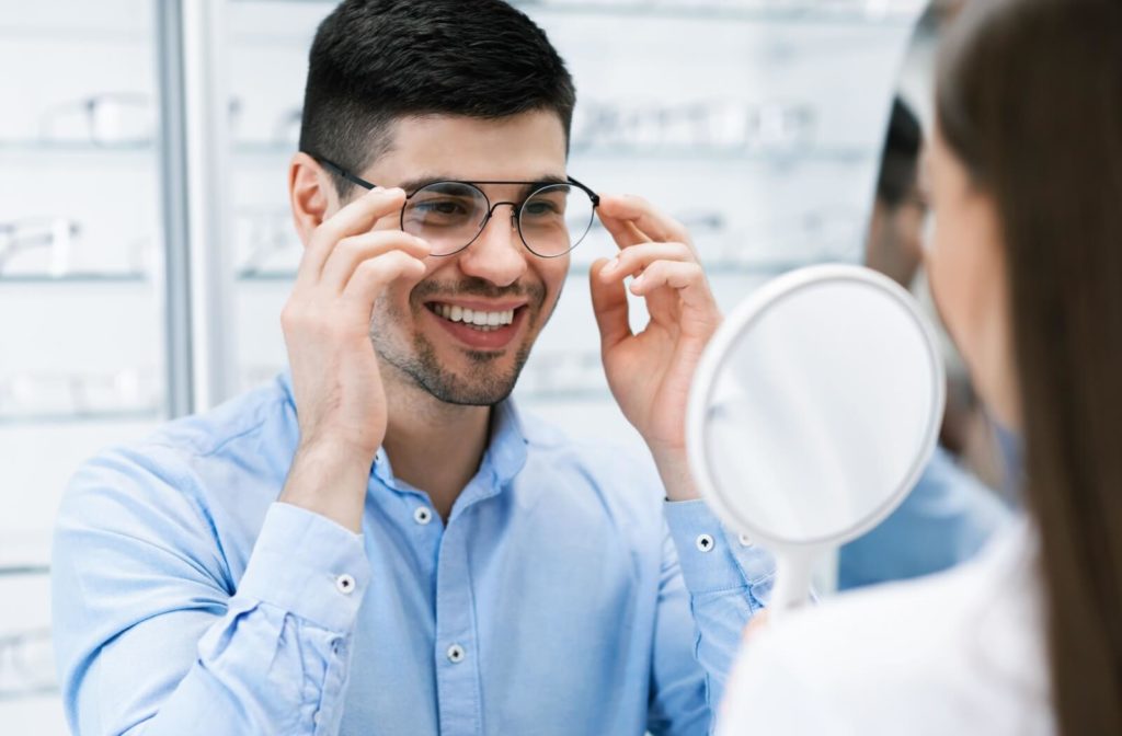 A young man trying on glasses at an optical store while being assisted by an optician.