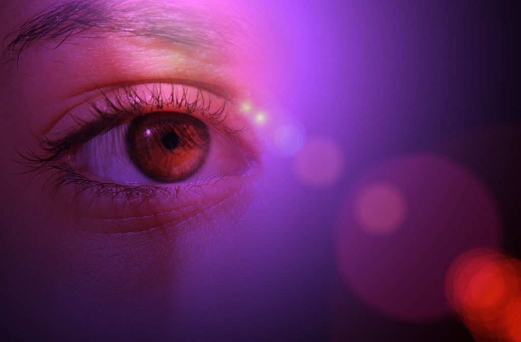 A close up of an eye with LED light shining in front, giving off a purple colour on the person's face.