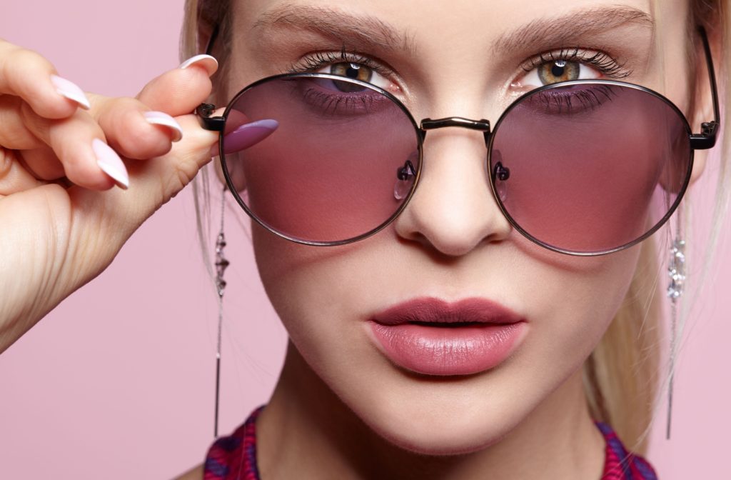 Close-up of a young woman looking into the camera while wearing rose-tinted lenses to combat migraine triggers