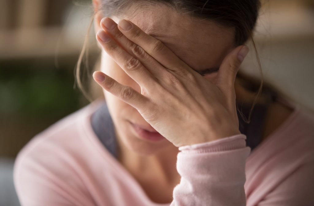 A woman with her hand covering her face due to a headache caused by eye strain.