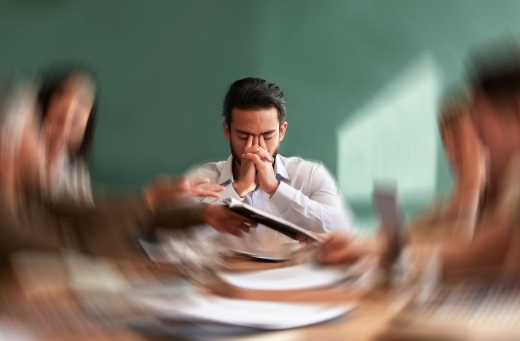 A person with visual vertigo sits with their head in their hands while the scene around them becomes blurry.