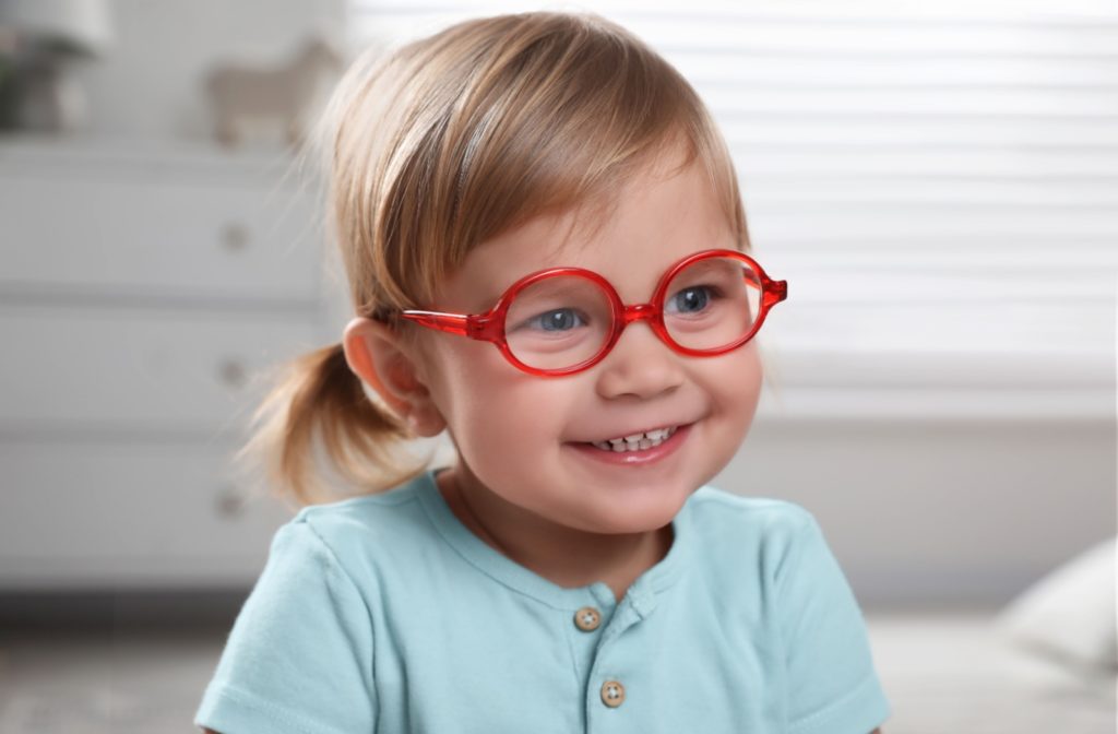 A young child wearing bright red glasses with MiYOSMART lenses giggles and plays in her room.