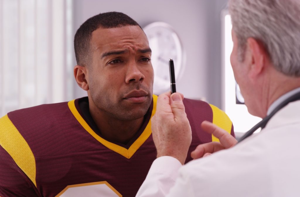 An optometrist has a football player with a concussion visually follow their pen to assess their vision.