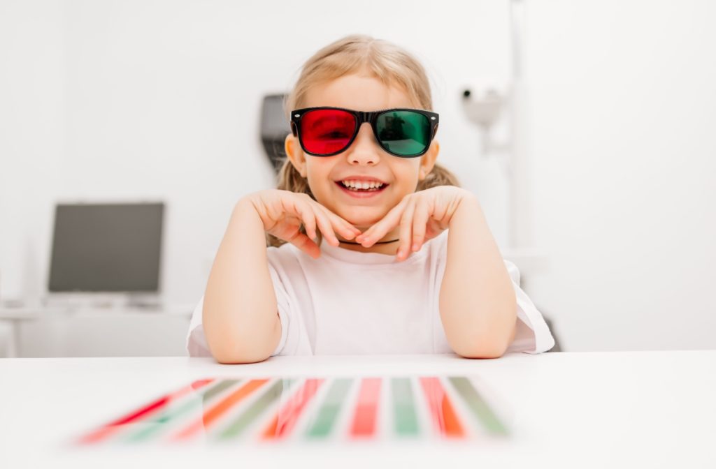 A young child smiles while wearing a pair of dual-coloured glasses during a visual training appointment.