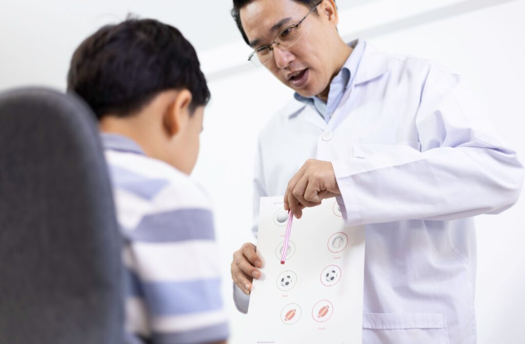 An optometrist holding a paper with icons on it helping a child during visual therapy improve visual perception.