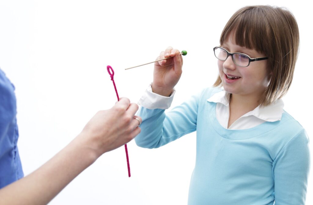 A child in front of a white background using a needle during visual perception therapy.