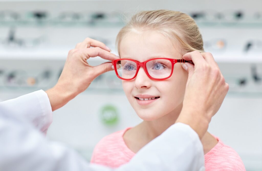 Child being fitted with red eyeglasses by an optician in a bright eyewear store
