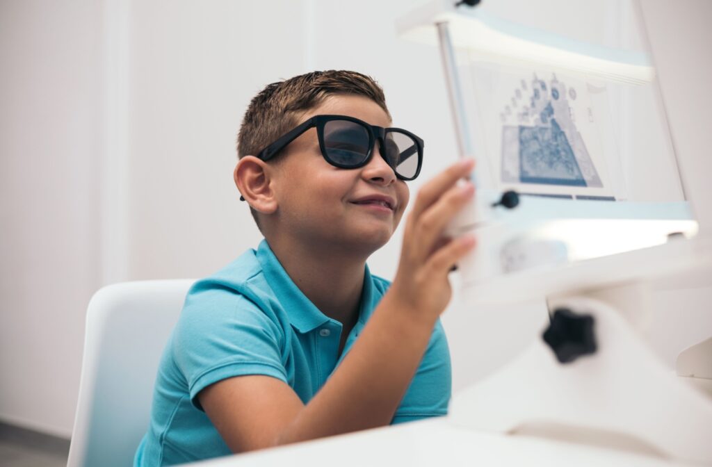 A young boy wearing specialized glasses smiles while participating in a vision therapy activity, interacting with a visual training device in a clinical setting.
