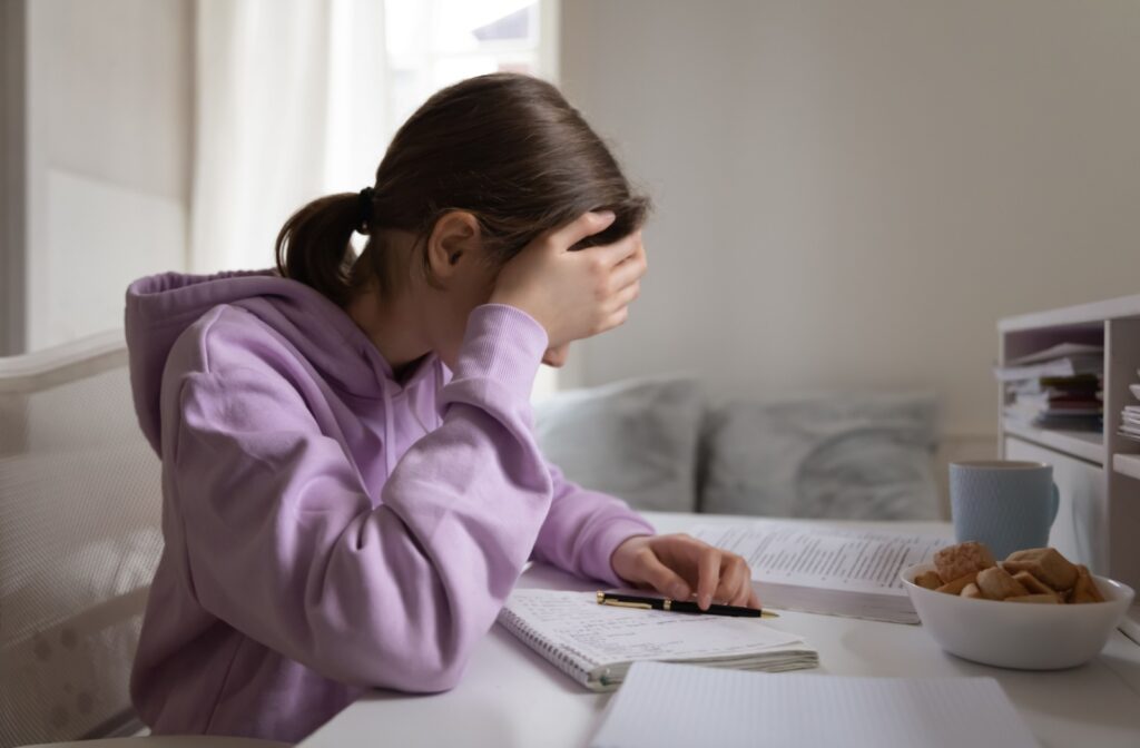 Young girl sits at a desk with her head resting aginst her hand