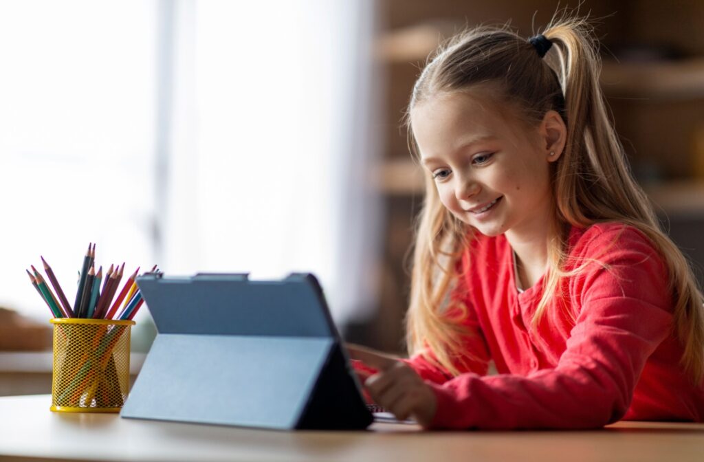 A young child smiles while they look at an ipad they are using.