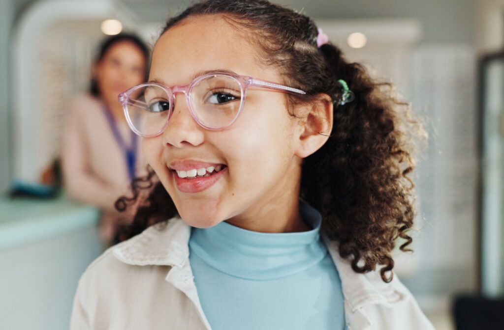 A young child wearing a pair of pink glasses has their head tilted to the side smiling