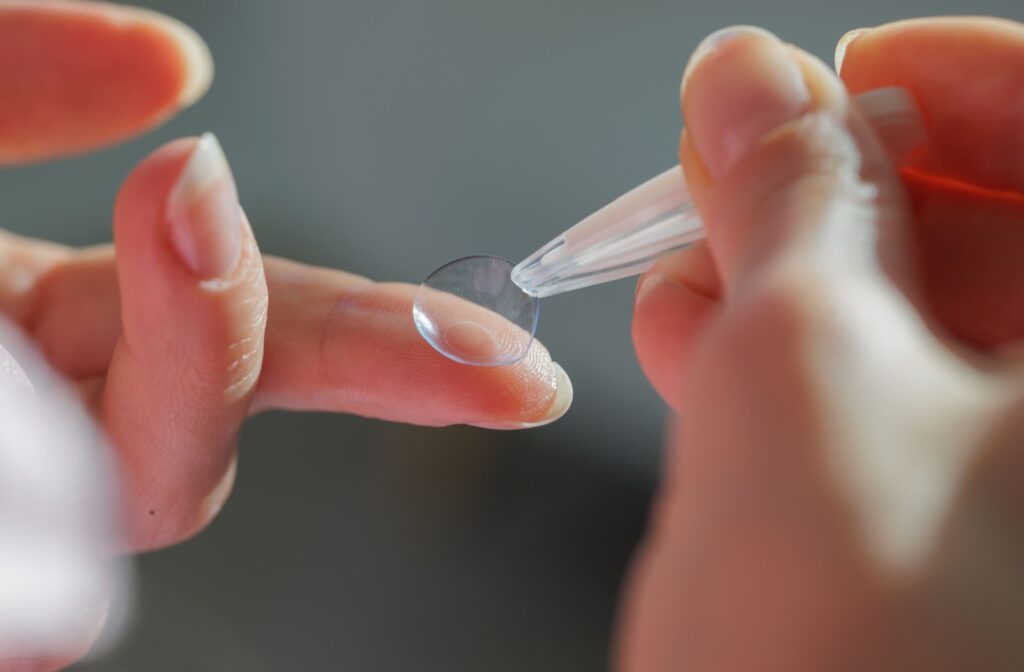 A close up of contact lens tweezers picking up a contact lens off of a finger