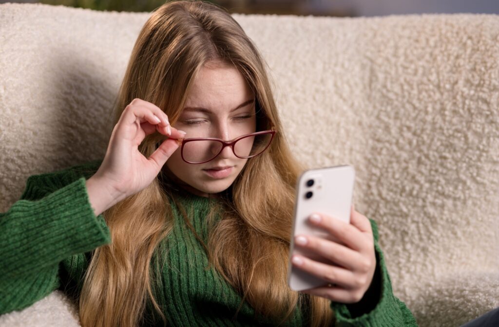 A person pulls their glasses lowers to look at their phone